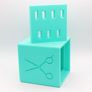May include: A turquoise blue plastic storage box with a cutout design of scissors on the front. The box has a separate lid with multiple slots for holding small items.