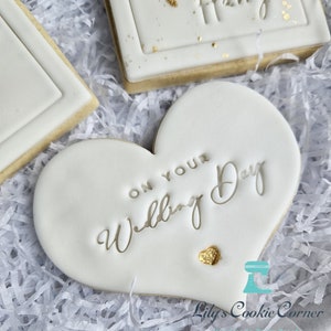 Pode incluir: Biscoitos brancos com glac&ecirc;, detalhes dourados e texto. Um biscoito em forma de cora&ccedil;&atilde;o diz "On Your Wedding Day". Outro biscoito tem o nome "Harry" em relevo. Os biscoitos est&atilde;o sobre papel branco.