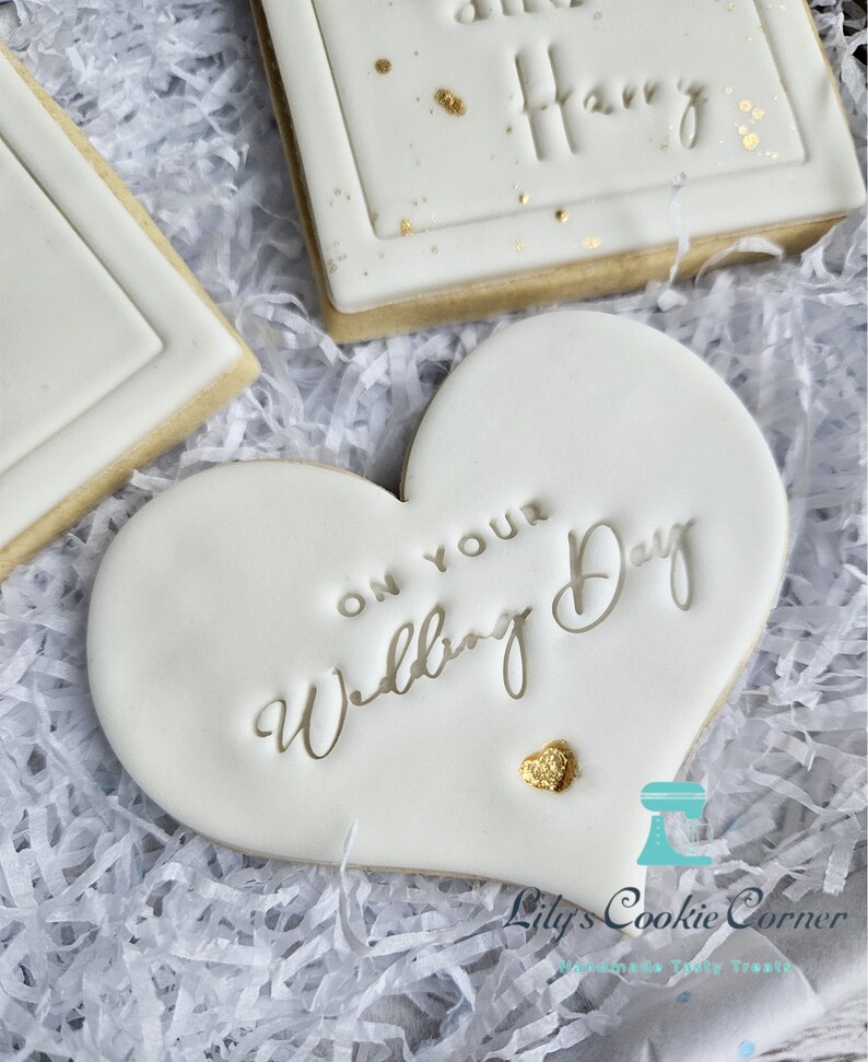 Pode incluir: Biscoitos brancos com glac&ecirc;, detalhes dourados e texto. Um biscoito em forma de cora&ccedil;&atilde;o diz "On Your Wedding Day". Outro biscoito tem o nome "Harry" em relevo. Os biscoitos est&atilde;o sobre papel branco.
