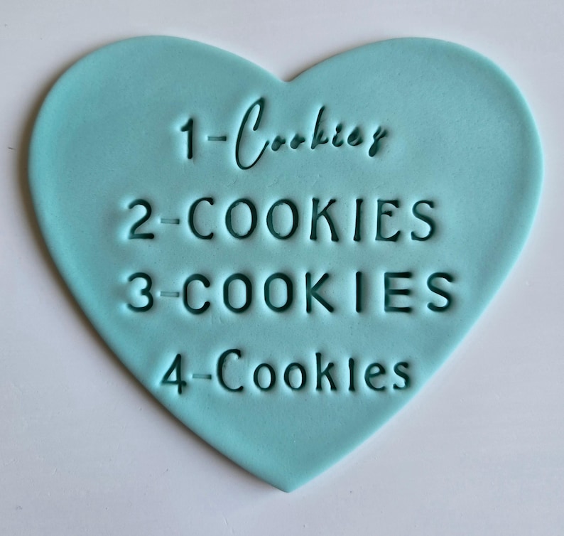 May include: A light blue heart-shaped cookie cutter with the words "1-Cookies", "2-COOKIES", "3-COOKIES", and "4-Cookies" embossed on the surface. The cookie cutter is made of a smooth material and is designed for baking.