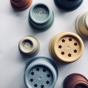 May include: Set of colorful stacking cups with different designs, including a rainbow, a cloud, stars, and a smiley face. The cups are made of silicone and are perfect for bath time or playtime.