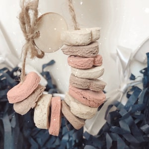 May include: A string of beige, pink and brown heart-shaped chew toys for dogs. The toys are strung together with twine and a wooden tag.