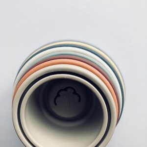 May include: A set of stacking rings in various shades of brown, gray, and beige. The rings are made of silicone and have a smooth, matte finish. The rings are stacked in a tower, with the largest ring at the bottom and the smallest ring at the top. The rings are designed for babies and toddlers to play with and help them develop their fine motor skills.