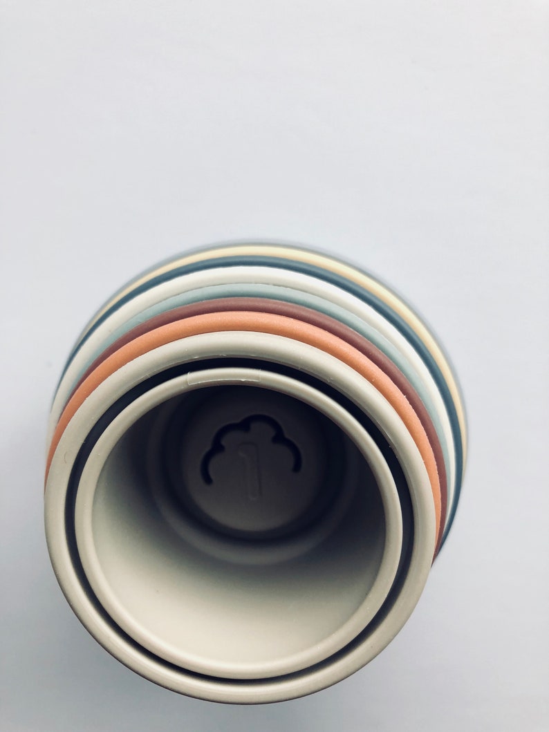 May include: A set of stacking rings in various shades of brown, gray, and beige. The rings are made of silicone and have a smooth, matte finish. The rings are stacked in a tower, with the largest ring at the bottom and the smallest ring at the top. The rings are designed for babies and toddlers to play with and help them develop their fine motor skills.
