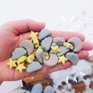 Könnte beinhalten: Eine Hand hält eine Vielzahl von bunten Sternen-, Mond- und Wolkenförmigen Süßigkeiten. Die Süßigkeiten sind aus einem weichen, teigigen Material hergestellt und perfekt für einen lustigen und festlichen Leckerbissen.