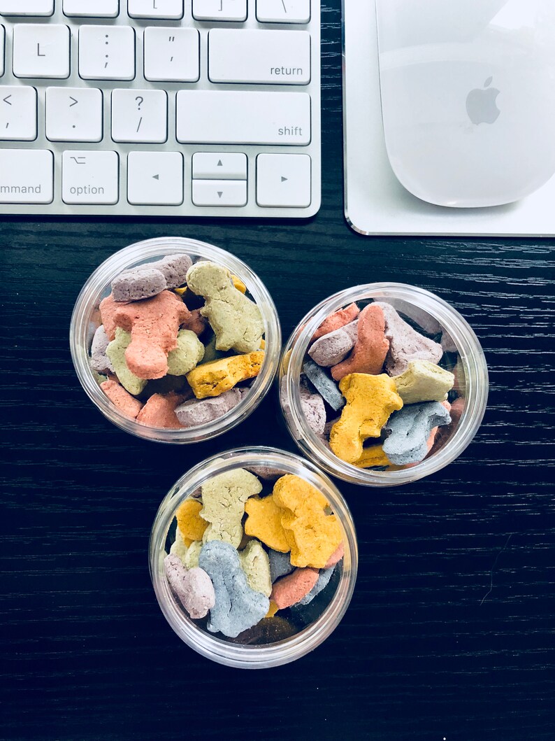 Puede incluir: Tres tarros de vidrio transparente llenos de galletas con forma de animales de colores. Las galletas son de color rosa, amarillo, azul y verde.