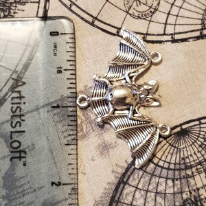 May include: Silver-toned metal bat charm with a detailed design. The charm is approximately 1 inch in length and has three jump rings for attaching to jewelry or other crafts.