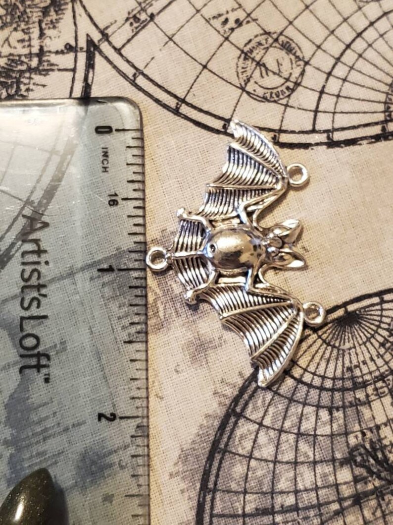 May include: Silver-toned metal bat charm with a detailed design. The charm is approximately 1 inch in length and has three jump rings for attaching to jewelry or other crafts.
