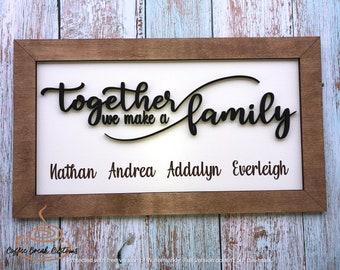 May include: A wooden framed sign with the text "Together we make a family" in black cursive lettering. The names Nathan, Andrea, Addalyn, and Everleigh are listed below the text.