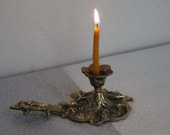 May include: A gold metal candle holder with an ornate design and a lit yellow candle.