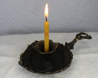 May include: A black metal candle holder with a decorative design and a yellow candle burning inside.