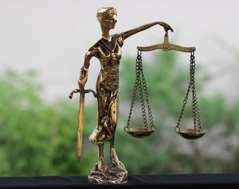 May include: A gold-colored statue of Lady Justice, blindfolded, holding a sword in one hand and scales in the other. The scales are balanced and the statue is standing on a base.