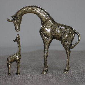May include: A pair of brass giraffe figurines. The larger giraffe is standing with its head bent down, while the smaller giraffe is standing upright. Both giraffes have a detailed, textured surface.