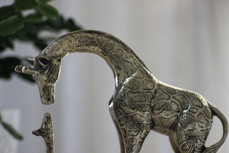 May include: A silver metal giraffe figurine with a detailed patterned design. The giraffe is standing on its hind legs with its head bent down.
