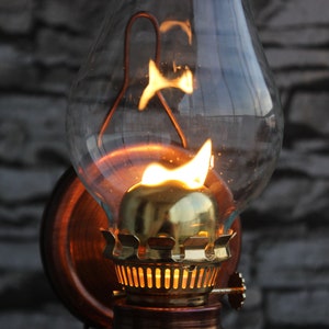 Puede incluir: Una l&aacute;mpara de aceite vintage con una chimenea de vidrio y un quemador de lat&oacute;n. La l&aacute;mpara est&aacute; encendida y la llama es visible dentro de la chimenea.