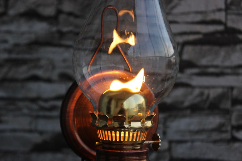 Puede incluir: Una l&aacute;mpara de aceite vintage con una chimenea de vidrio y un quemador de lat&oacute;n. La l&aacute;mpara est&aacute; encendida y la llama es visible dentro de la chimenea.