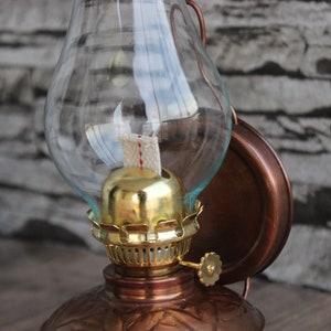 Puede incluir: Una l&aacute;mpara de aceite de cobre con una chimenea de vidrio y un quemador dorado. La l&aacute;mpara est&aacute; montada en una pared y tiene un dise&ntilde;o decorativo.