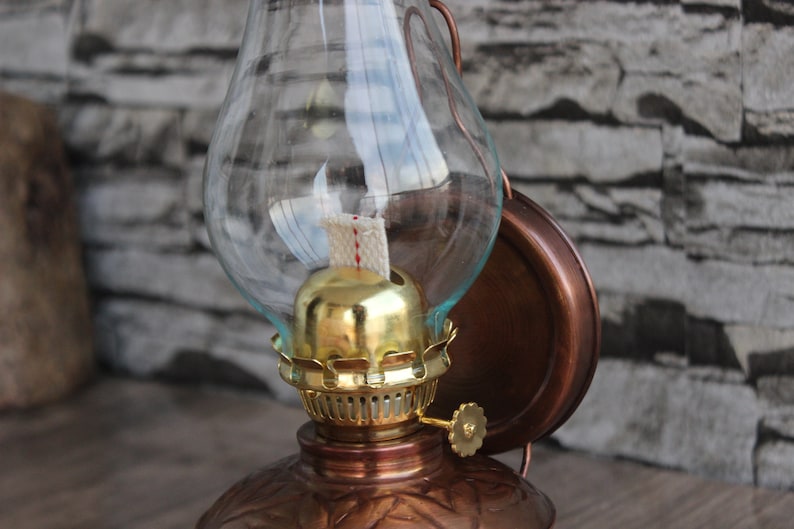 Puede incluir: Una l&aacute;mpara de aceite de cobre con una chimenea de vidrio y un quemador dorado. La l&aacute;mpara est&aacute; montada en una pared y tiene un dise&ntilde;o decorativo.