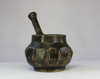 May include: A small, dark brown, brass mortar and pestle with a textured, faceted design. The mortar has a round, bulbous shape and the pestle is cylindrical.