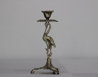 May include: A silver metal candlestick with a crane design. The crane is standing on a base with three legs. The candlestick is about 10 inches tall.