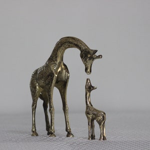 May include: A pair of brass giraffe figurines, one larger than the other, with intricate details. The larger giraffe is looking down at the smaller one.