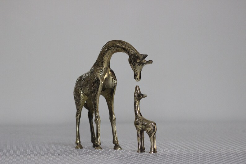 May include: A pair of brass giraffe figurines, one larger than the other, with intricate details. The larger giraffe is looking down at the smaller one.