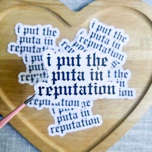 May include: A collection of white die-cut stickers featuring the dark blue text "i put the puta in reputation" written in a gothic-style font. The stickers are arranged in a stack, with one prominent sticker held up by a thin pink tool.