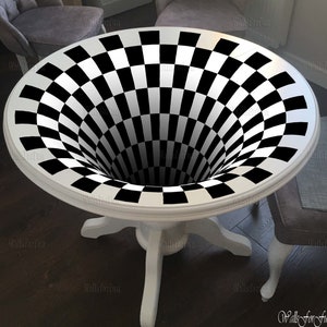 Peut inclure: Une table blanche avec un plateau en damier noir et blanc qui crée une illusion d'optique de vortex tourbillonnant. La table a un plateau rond et trois pieds.