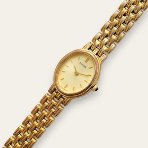 May include: A gold-coloured Pulsar watch with an oval face and a matching gold link strap. The watch face is cream-coloured with gold hands and markers. The strap is made of small, rectangular links.