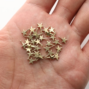 May include: A pile of small gold star-shaped metal charms in the palm of a hand.