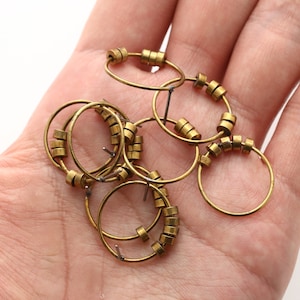 Puede incluir: Un conjunto de seis pendientes de aro dorados con pequeñas cuentas redondas. Los aros están hechos de metal fino y las cuentas están espaciadas uniformemente alrededor de los aros.