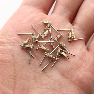 May include: A selection of small, gold-coloured earring posts with rectangular, clear crystal accents. The earrings have a post and loop design, suitable for jewellery making or crafting. The earrings are displayed on a light background.
