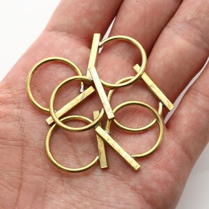 Puede incluir: Un conjunto de anillos y barras metálicas de color dorado. Los anillos son circulares y las barras son rectas, que se cruzan con los anillos en varios puntos. Los objetos están dispuestos en un grupo, creando un diseño abstracto. Los artículos se sostienen en una mano.