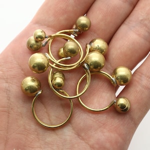 May include: A set of gold-toned metal rings with round balls on each end. The rings are linked together and are lying on a hand.