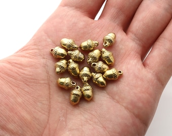 May include: A pile of gold-colored acorn charms with a loop for hanging. The charms are about 1 inch in size and have a detailed acorn design.