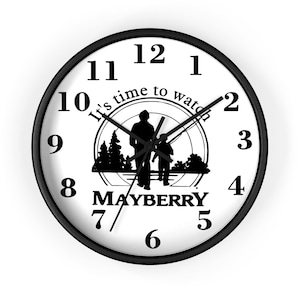 May include: A round wall clock with a black frame and a white face. The clock features black numerals, hands, and the text "It's time to watch" and "MAYBERRY". A silhouette of two people walking is in the center.