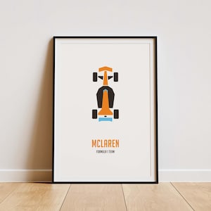 May include: A framed print showing a top-down view of a McLaren Formula 1 race car in orange, black, and light blue. The word "MCLAREN" is printed below the car, with "FORMULA 1 TEAM" underneath. The print is in a black frame.