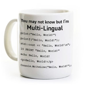 May include: A white ceramic mug featuring black text that reads: You may not know but I'm Multi-Lingual, followed by various programming code snippets for printing Hello, World! in different languages including Python, C, C++, BASIC, PHP, HTML, and C#.