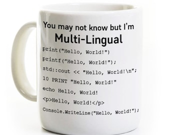 May include: A white ceramic mug featuring black text that reads: You may not know but I'm Multi-Lingual, followed by various programming code snippets for printing Hello, World! in different languages including Python, C, C++, BASIC, PHP, HTML, and C#.