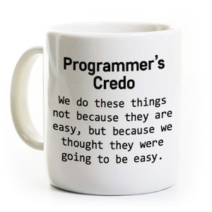 May include: White ceramic mug with black text that reads "Programmer's Credo" and "We do these things not because they are easy, but because we thought they were going to be easy."