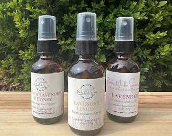 May include: Three glass spray bottles with black tops and labels. The labels are white with pink and purple text. The bottles contain room and linen spray in the scents Lavender Lemon, French Lavender & Honey, and Lavender. Each bottle is 2 oz.