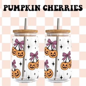 Puede incluir: Dos vasos de cristal transparente con tapas de bambú y pajitas de metal, con un patrón de calabazas naranjas con lazos morados y estrellas negras. El texto PUMPKIN CHERRIES está impreso en negro sobre los vasos.