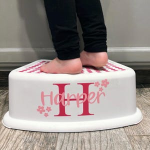 May include: White step stool with pink polka dots and the name "Harper" in pink lettering with a large red "H" in the center. A child is standing on the stool.