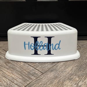 May include: White plastic step stool with black polka dots on the top and the name "Holland" with two black "H"s in a blue font.