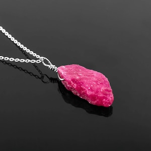 May include: A silver chain necklace with a raw pink ruby pendant. The ruby is a natural, rough stone with a deep pink color.