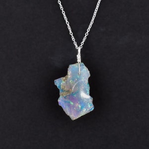 May include: A silver chain necklace with a pendant made from a large, iridescent, blue and purple opal. The opal is irregularly shaped and has a rough, natural texture.