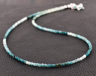 May include: A delicate necklace made of graduated blue gemstone beads. The beads range in color from light blue to dark green, creating a beautiful ombre effect. The necklace is finished with a silver clasp.