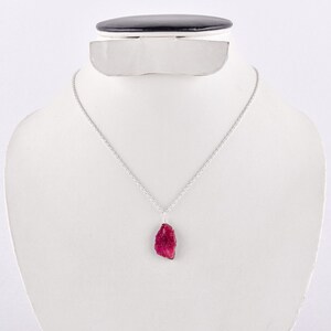 May include: A silver chain necklace with a raw, red ruby pendant. The ruby is a deep red color and has a natural, unpolished look.