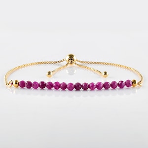 May include: A gold chain bracelet with a sliding clasp and a row of pink gemstone beads.