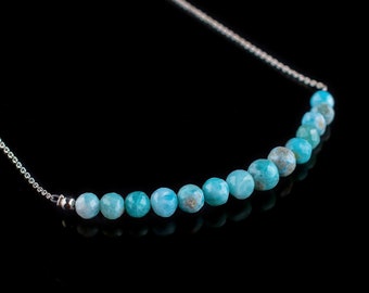 May include: A silver chain necklace with a row of light blue gemstone beads.